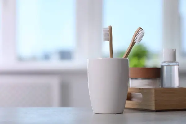 Bamboo toothbrushes in holder and cosmetic products on light grey table. Space for text