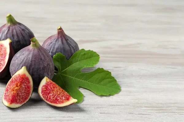 Whole and cut ripe figs with leaf on light wooden table, closeup. Space for text