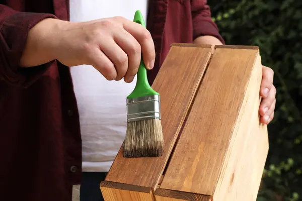 Man applying wood stain onto crate outdoors, closeup