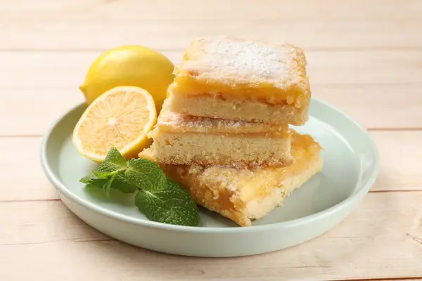 Tasty lemon bars with powdered sugar and mint on wooden table, closeup