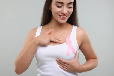 Açık gri arka planda pembe kurdeleli güzel bir genç kadın. Göğüs kanseri farkındalığı