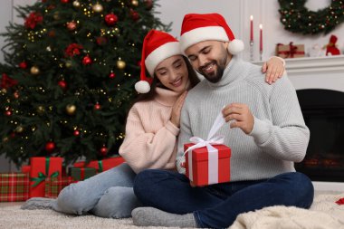 Noel Baba şapkalı mutlu kadın evde erkek arkadaşına Noel hediyesini sunuyor.