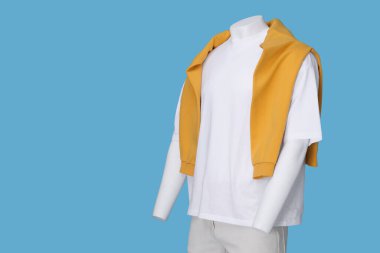 Beyaz tişört giymiş erkek manken, şık şort ve açık mavi arka planda turuncu süveter, metin için yer