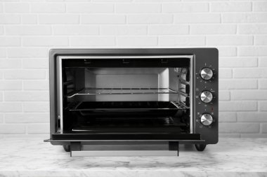 Tuğla duvarın yanındaki beyaz mermer masada bir elektrikli fırın.