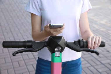 Dışarıdaki elektrikli scooter 'ın engelini kaldırmak ve ödemek için akıllı telefon kullanan bir kadın.