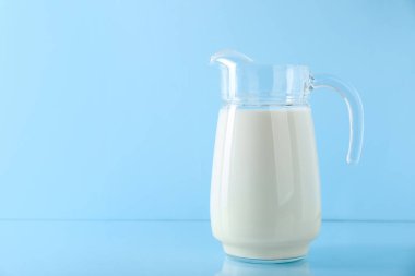 Açık mavi arkaplanda bir sürahi taze süt, metin için boşluk