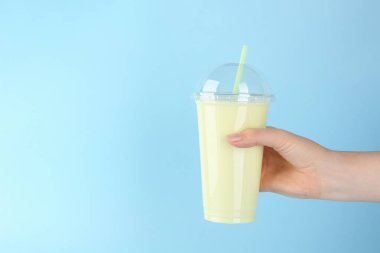 Açık mavi arka planda plastik bardakta lezzetli meyve püresi olan kadın, yakın plan. Metin için boşluk