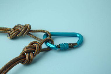 Açık mavi arka planda ipleri olan bir metal karabina, yakın plan.