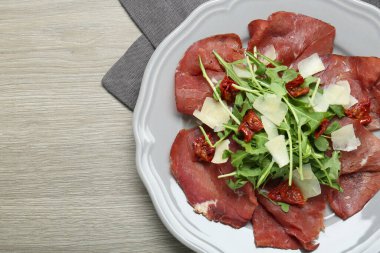 Tabak dolusu lezzetli Bresaola salatası, kurutulmuş domates ve ahşap masa üzerinde parmesan peyniri. Metin için boşluk