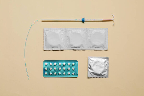 Выбор контрацепции. Таблетки, презервативы и внутриутробное устройство на бежевом фоне, плоская укладка