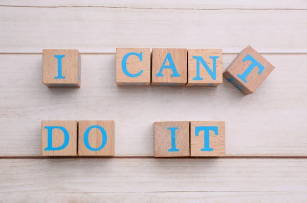 Motivation concept. Changing phrase from I Can\'t Do It into I Can Do It by removing cube with letter T on light wooden table, flat lay