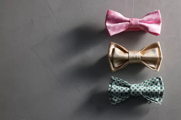 Stylish color bow ties on gray textured background, flat lay. Space for text