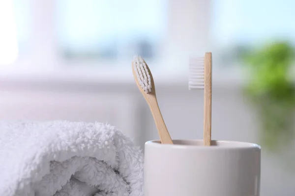 Bamboo toothbrushes in holder and towel on blurred background, closeup