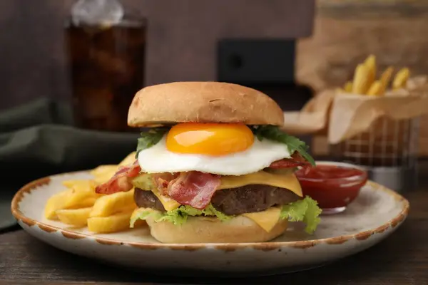 Delicious burger with fried egg and french fries served on wooden table, closeup