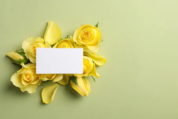 Beautiful yellow roses, petals and blank card on light olive background, flat lay. Space for text