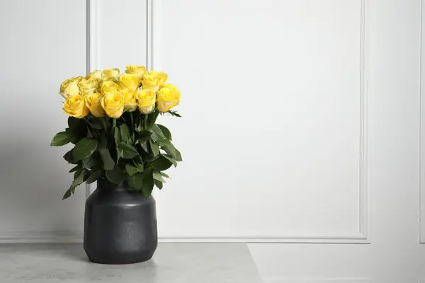 Beautiful bouquet of yellow roses in vase on light grey table near white wall, space for text
