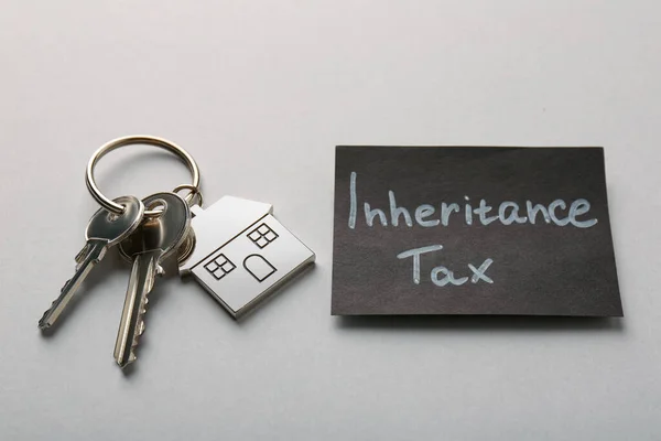 Card with phrase Inheritance Tax and keys with house shaped key chain on grey background