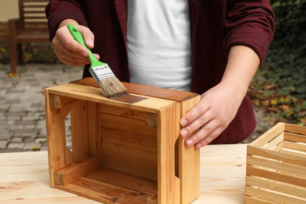 Man applying wood stain onto crate at table outdoors, closeup