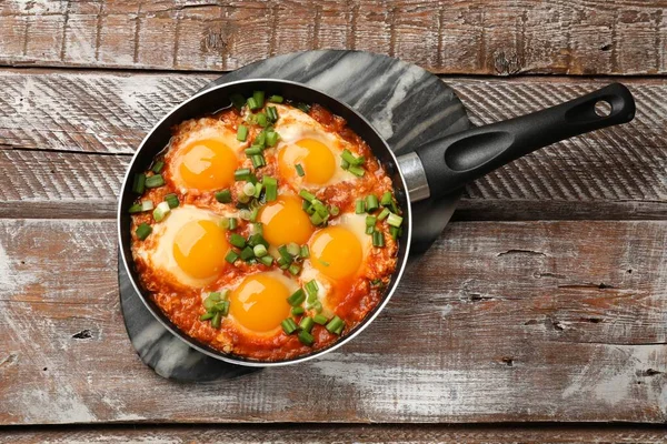 Delicious Shakshuka in frying pan on wooden table, top view