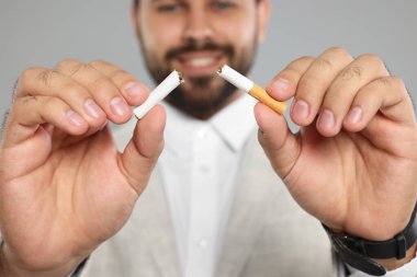 Sigara içmeyi bırak. Açık gri arka planda sigara kıran adam, seçici odak