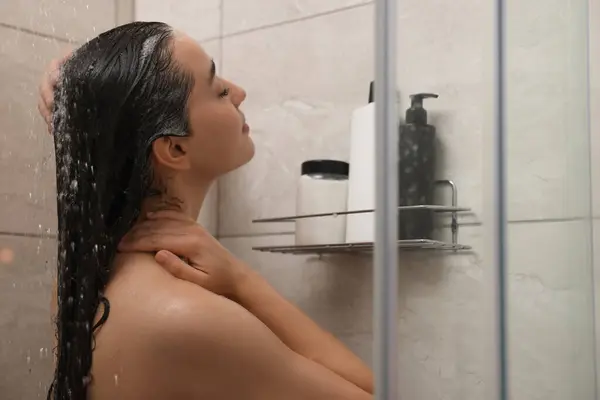 Woman washing hair in shower stall indoors
