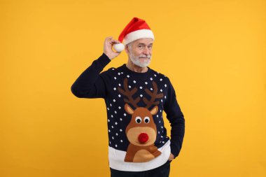 Noel süveteri ve turuncu arka planda Noel Baba şapkası giyen son sınıf öğrencisi.