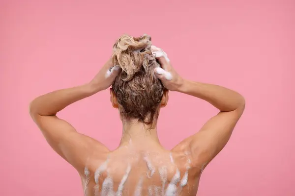 Woman washing hair on pink background, back view