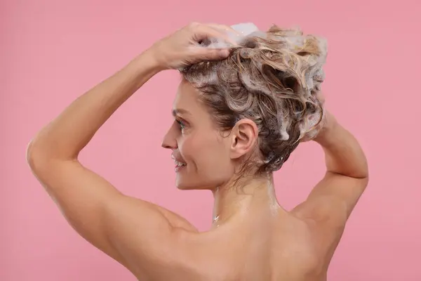 Beautiful happy woman washing hair on pink background
