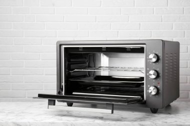 Tuğla duvarın yanındaki beyaz mermer masada bir elektrikli fırın.