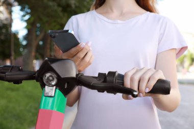 Dışarıdaki elektrikli scooter 'ın engelini kaldırmak ve ödemek için akıllı telefon kullanan bir kadın.