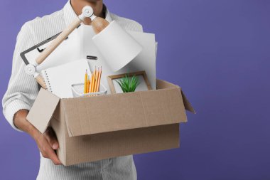 Mor arka planda kişisel ofis eşyalarıyla dolu kutusuyla işsiz genç adam, yakın plan. Metin için boşluk