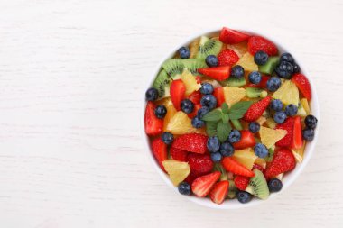 Beyaz ahşap masadaki kasede taze meyve salatası, üst manzara. Metin için boşluk