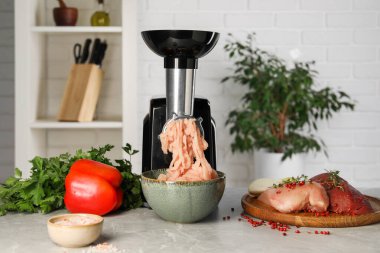 Elektrikli et öğütücü, içinde tavuk kıyması ve gri mermer masa üzerinde ürünler var.