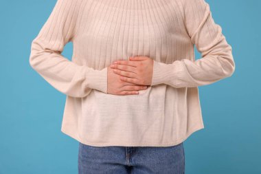 Woman suffering from abdominal pain on light blue background, closeup. Unhealthy stomach clipart