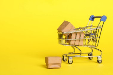 Sarı arka planda kutuları olan küçük metal alışveriş arabası. Metin için boşluk