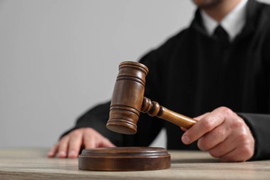 Tokmaklı yargıç, açık gri arka planda, ahşap masada oturuyor, yakın plan.