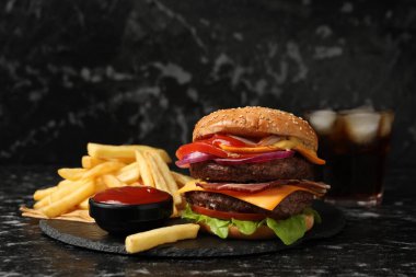 Köfteli lezzetli hamburger, patates kızartması ve siyah masada sos.