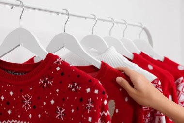Beyaz duvarın yanındaki askıdan Noel süveterini seçen kadın, yakın plan.