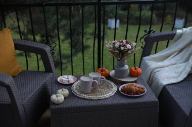 Terasta rattan mobilyalarla dinlen. İç, tatlı ve sonbahar dekoru masada.