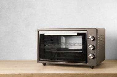 Açık mavi duvarın yanındaki ahşap masada bir elektrikli fırın.