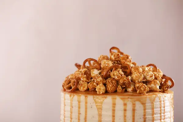 Caramel drip cake decorated with popcorn and pretzels against light background, closeup. Space for text
