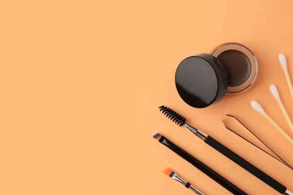Eyebrow pomade with henna effect and professional tools on orange background, flat lay. Space for text