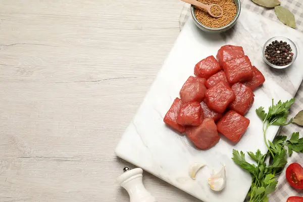 Raw beef meat and different ingredients for cooking delicious goulash on light wooden table, flat lay. Space for text