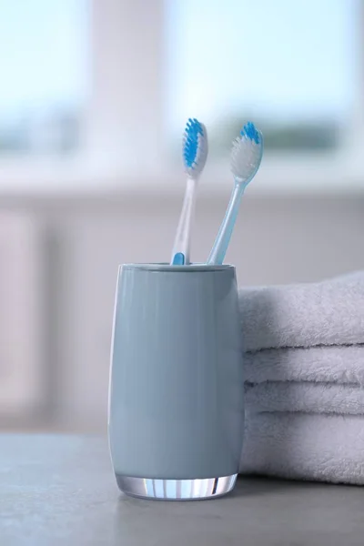 Plastic toothbrushes in holder and towels on light grey table