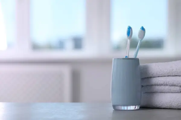 Plastic toothbrushes in holder and towels on light grey table indoors. Space for text