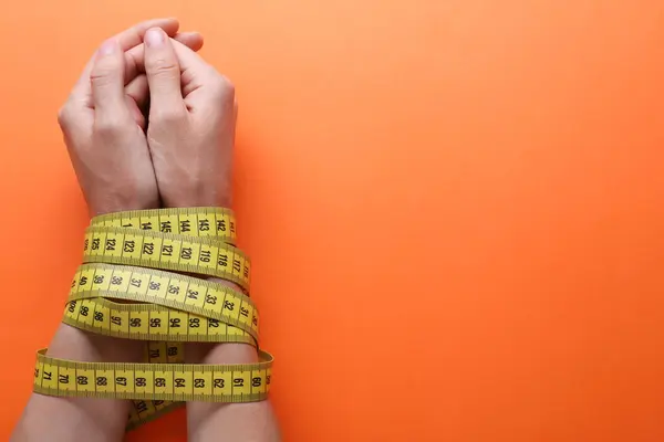 Woman tied with measuring tape on orange background, top view and space for text. Diet concept
