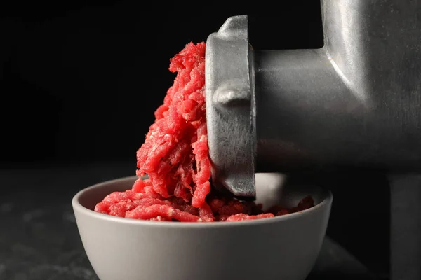 Mincing beef with metal meat grinder on black background, closeup