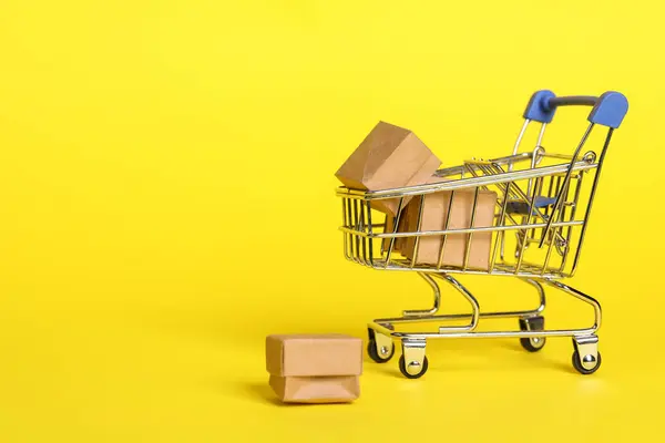 Small metal shopping cart with boxes on yellow background. Space for text