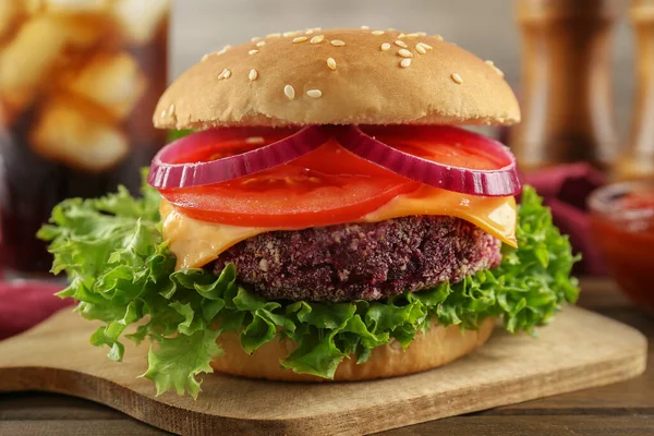 Tasty vegetarian burger with beet patty on wooden table, closeup