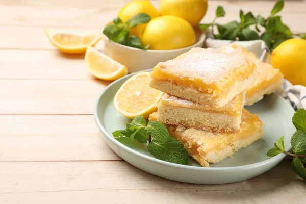 Tasty lemon bars with powdered sugar and mint on wooden table, closeup. Space for text
